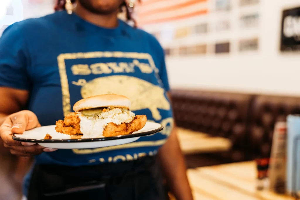 SAW's BBQ team member serving a fried chicken sandwich in a branded shirt